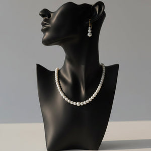A pearl necklace and matching drop earrings displayed on a round wood slice coaster, with pink flowers at the top and a gold card reading FASHION EARRINGS.